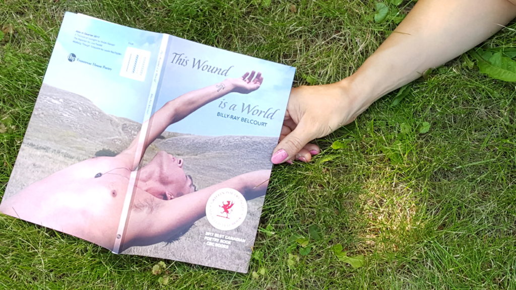 person holding the book The Wound is the World while laying in the grass